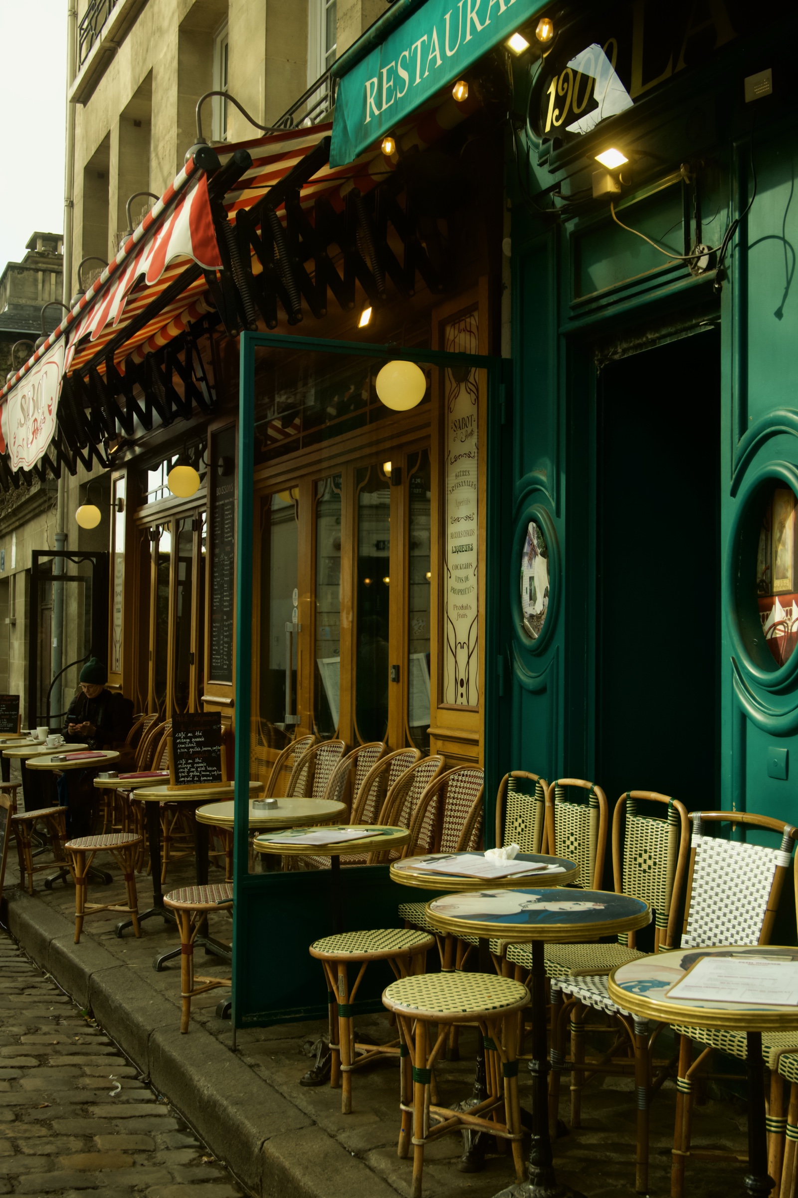 Empty rattan chairs outside a green Paris cafe
